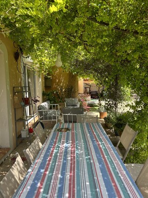 Ein überdachter Patio-Bereich mit gestreiftem Tischleinentuch, Gartenmöbeln und Topfpflanzen.