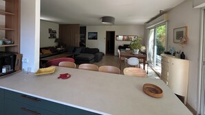 Eine moderne Küche mit Kochinsel, Essbereich mit Stühlen und ein Wohnzimmer mit Sofa und Fernseher.