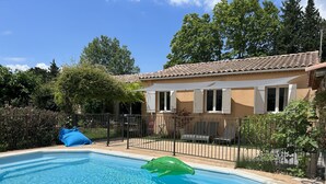 Ein Schwimmbad mit gefliestem Deck, einer umzäunten Terrasse und einem Gebäude mit einem gefliesten Dach und Fenstern.