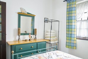 Un dormitorio con cama, cómoda con espejo, mesita de noche y ventana con cortinas.