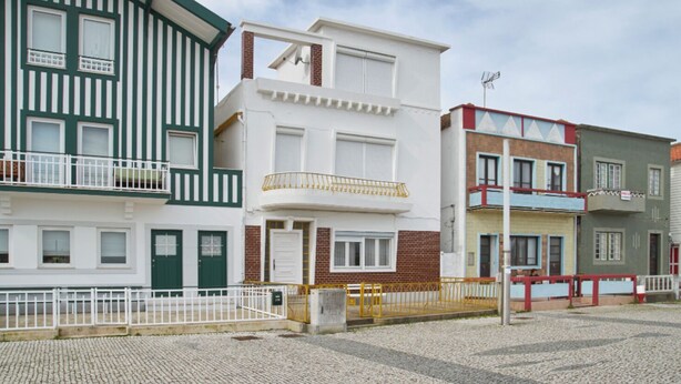 Uma fileira de edifícios residenciais com varandas, uma rua de calçada e céu claro.