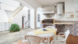Um pátio com mesa e cadeiras, uma pequena cozinha com churrasqueira e uma escadaria.