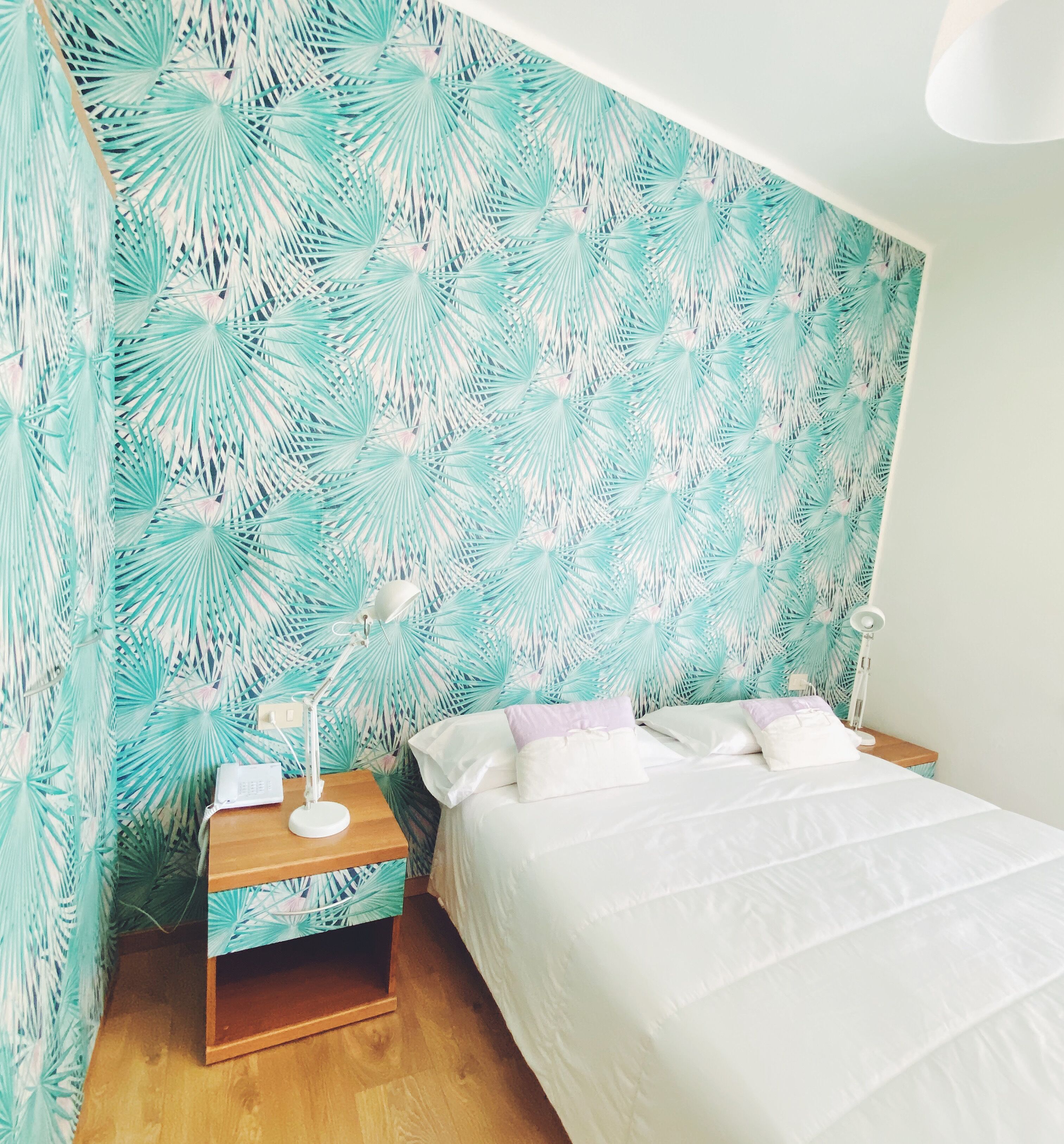 Un dormitorio con cama, mesitas de noche y una pared con estampado de hojas tropicales.