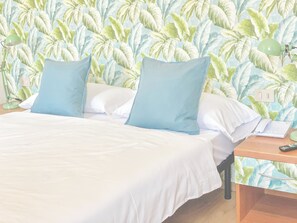 A bed with white bedding and two blue pillows, a nightstand with a lamp and a phone, and a wall with a leafy pattern. - L'Ennesima Osteria con Alloggio - Bike Hotel (Toscolano Maderno)