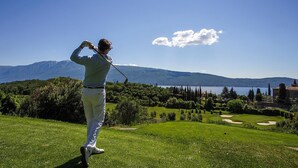 A golfer on a golf course with a view of mountains and a lake.