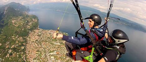 Una persona haciendo parapente con vistas a un pueblo costero y montañas al fondo.