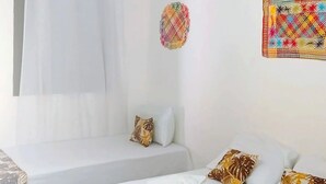 Une chambre d’hôtel avec deux lits, un luminaire suspendu, un élément décoratif mural et une fenêtre avec un rideau.
