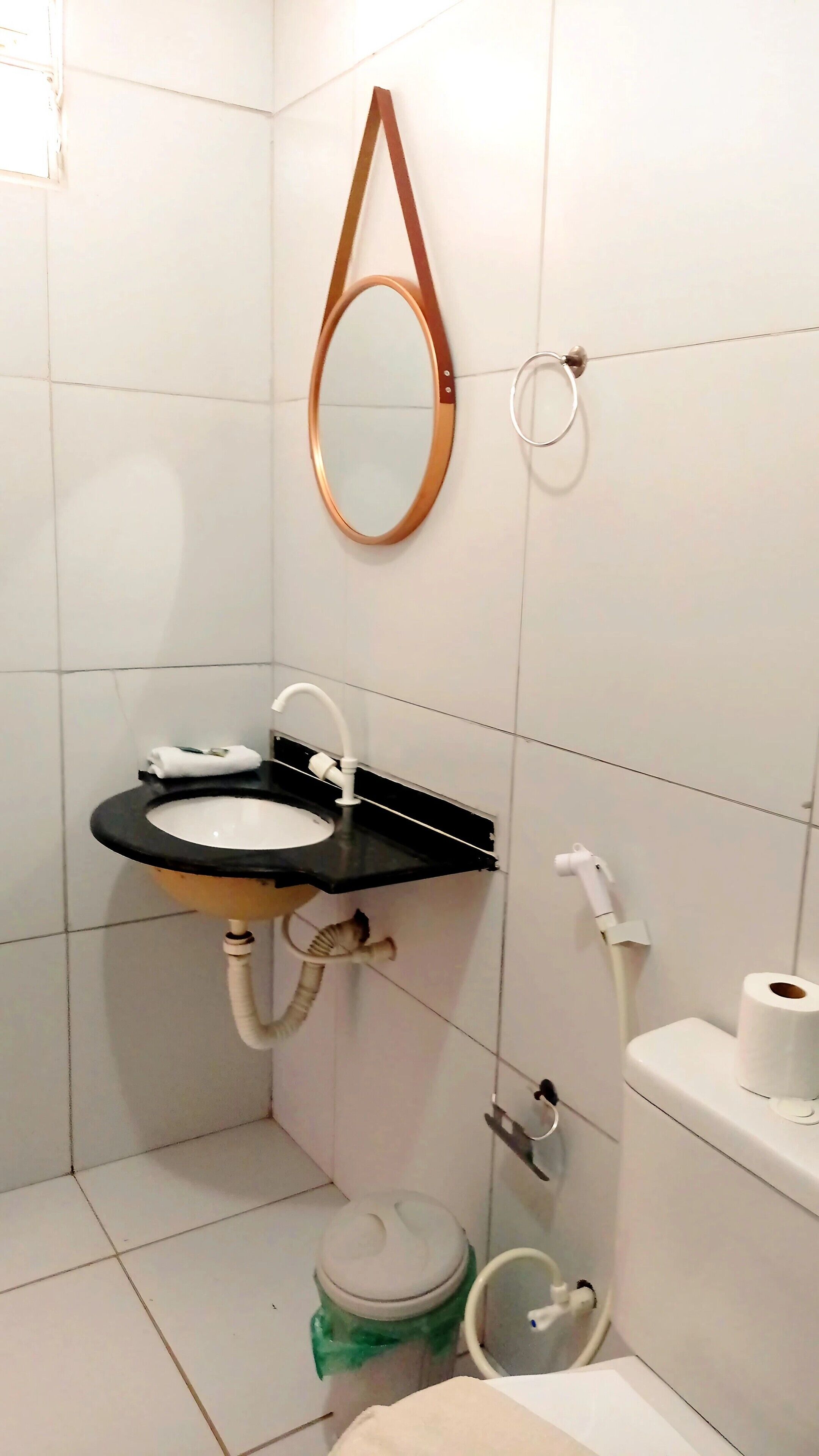 Une salle de bain avec un lavabo noir, des carreaux blancs, un miroir, des toilettes et une poubelle.