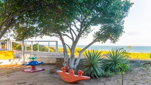 Une aire de jeux avec une balançoire et un manège, entourée d’arbres et offrant une vue sur la mer.