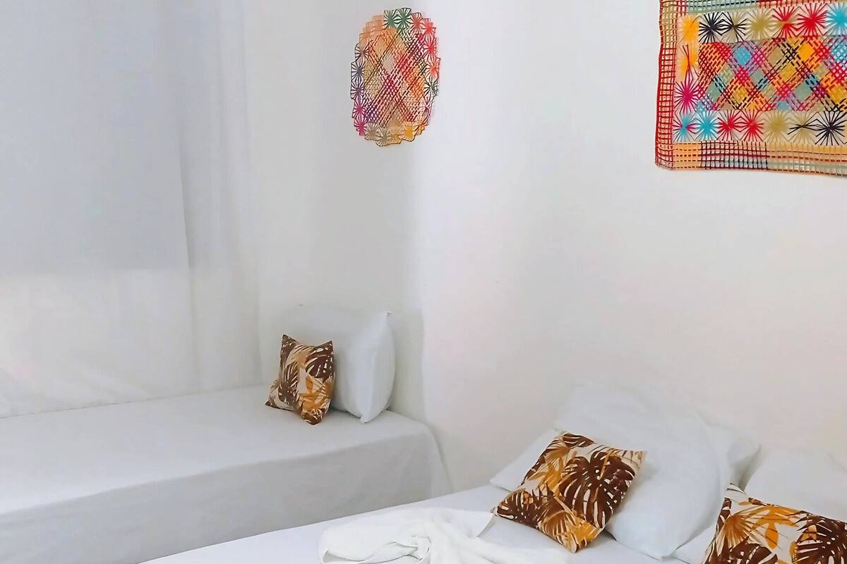 Une chambre d’hôtel avec un lit, un petit lit, un luminaire suspendu, un rideau et un élément décoratif mural.