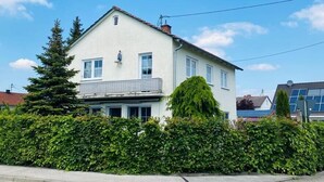 Une maison à deux étages, avec une façade blanche, une cheminée bien visible et un petit balcon.
