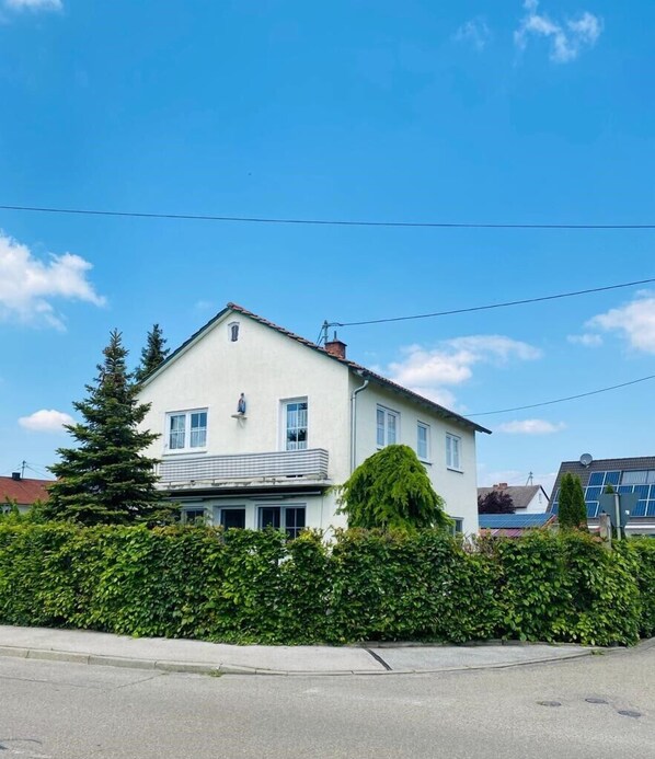 Een huis met twee verdiepingen, een witte gevel, een zichtbare schoorsteen en een klein balkon.