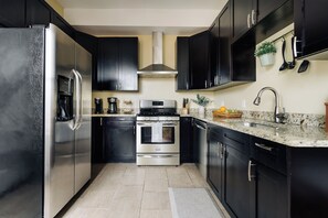A modern kitchen with dark cabinetry, stainless steel appliances, and a granite countertop.