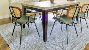 Uma sala de jantar com uma mesa grande, seis cadeiras, um candelabro, um armário branco e um vaso com planta.