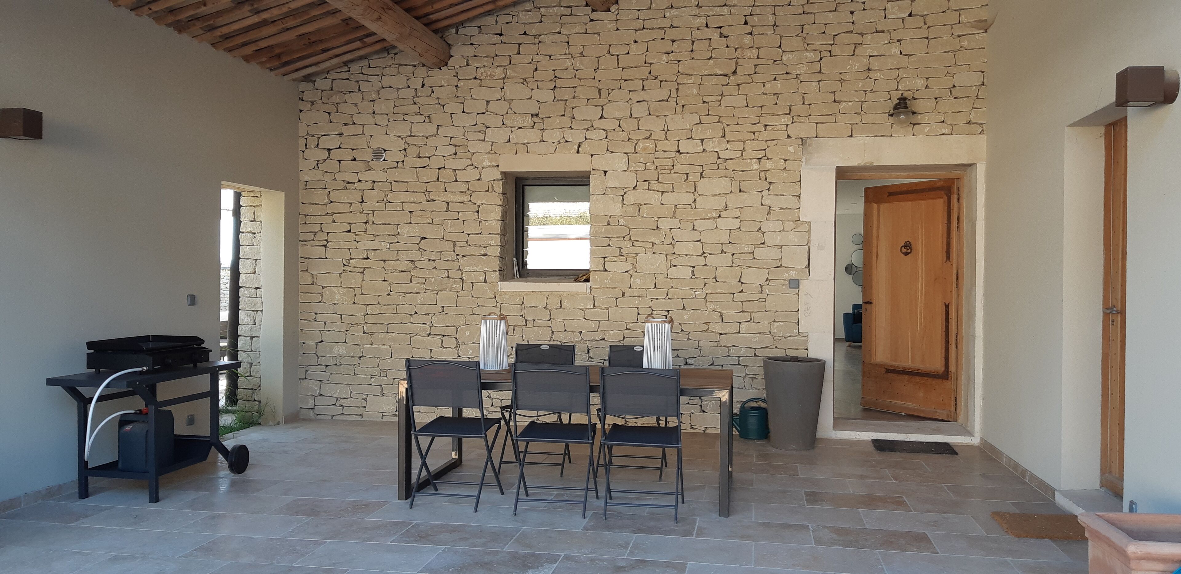 A stone-walled room with a table and chairs, a wooden door, and a window.
