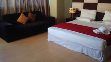 A hotel room with a bed, a sofa, a nightstand, and a lamp.