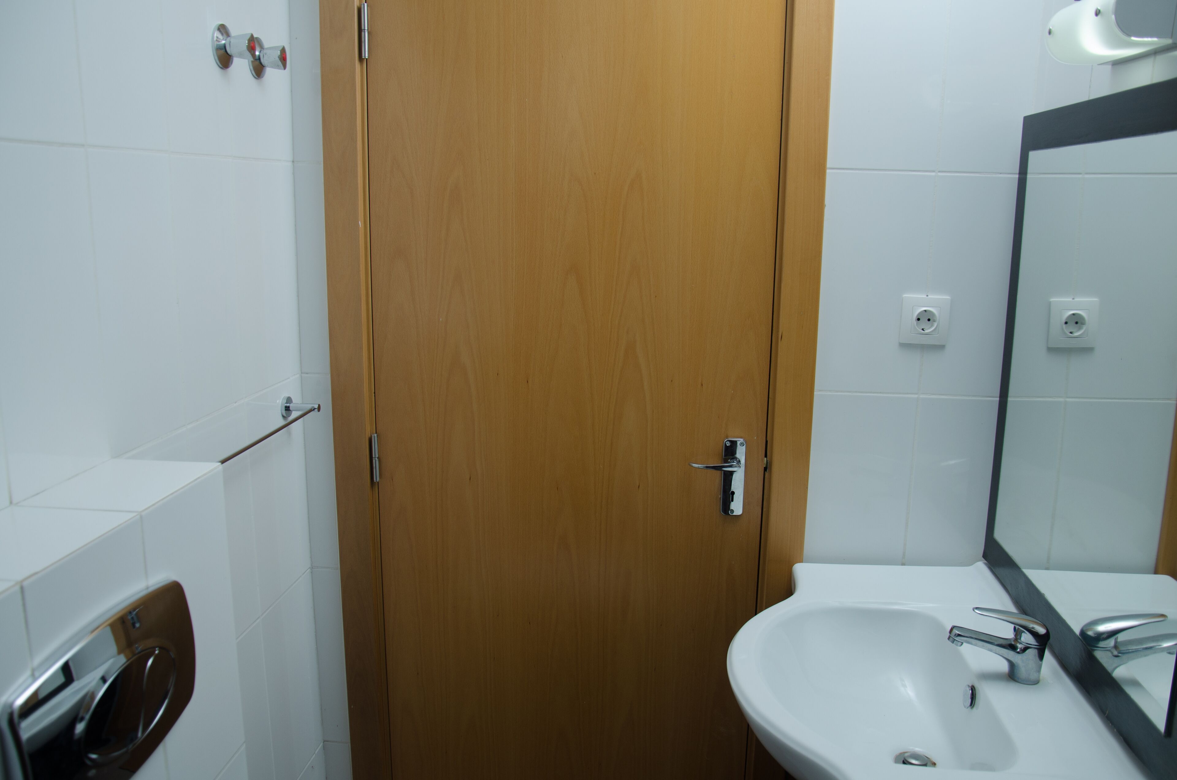 Un baño con una puerta de madera, un lavabo blanco y un espejo.