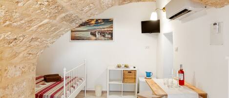 Una habitación acogedora con una cuna blanca, una mesita con una botella y vasos, un cuadro en la pared y un equipo de aire acondicionado blanco.