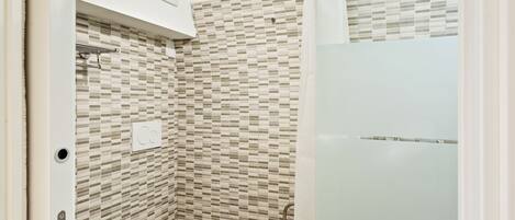Une petite salle de bain avec des toilettes, une douche et un mur carrelé.