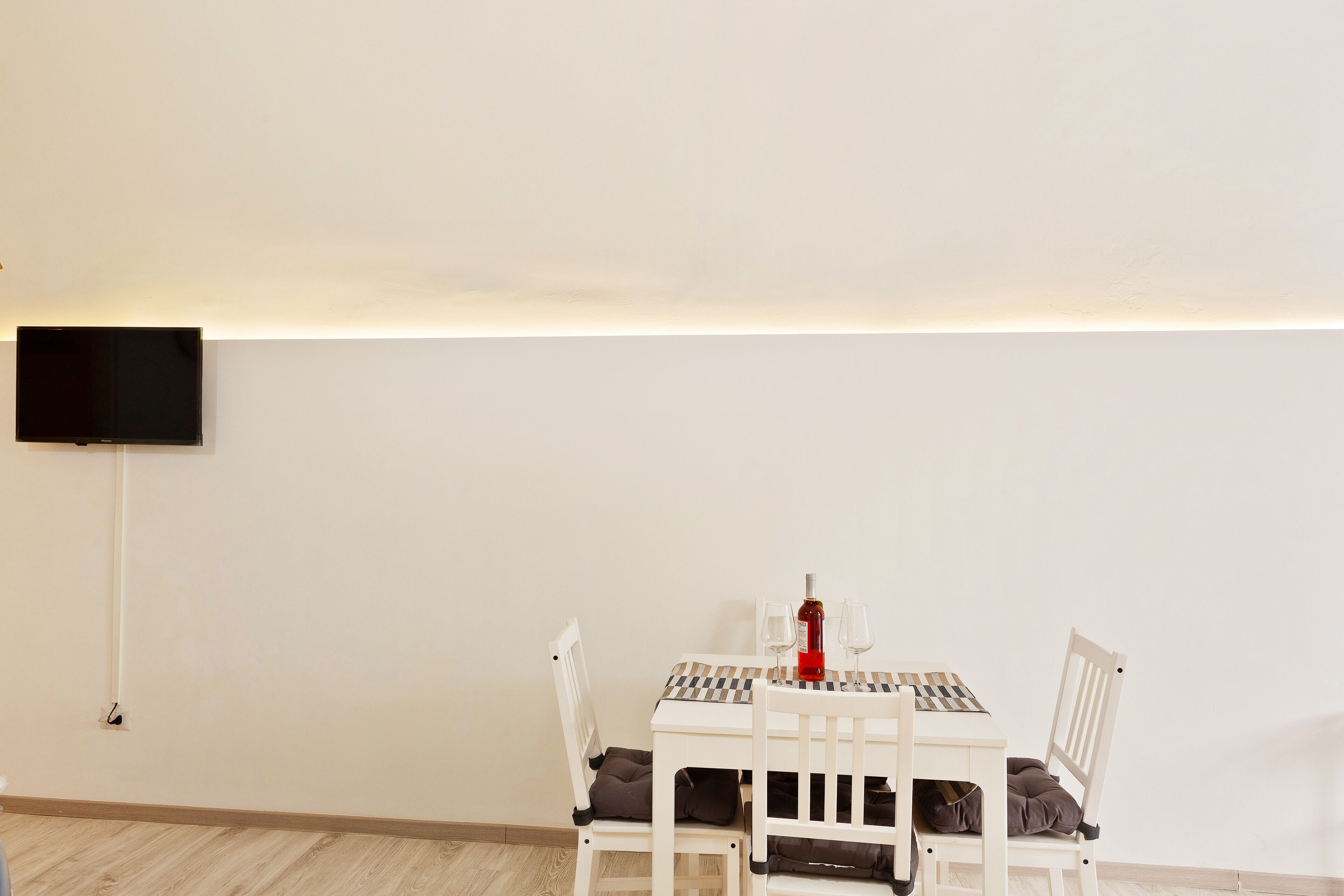 A dining area with a table set for two, a television mounted on the wall, and a wooden floor.