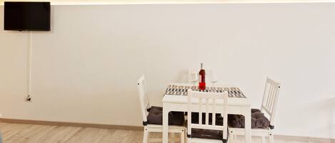 A dining area with a table set for two, a television mounted on the wall, and a wooden floor.