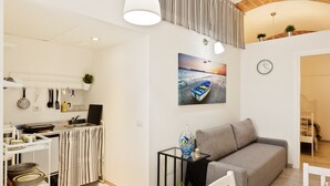 A modern kitchen with a dining area, a sofa, and a painting of a boat on a beach. - San Nicola Casa Clemente Apartment (Bari)