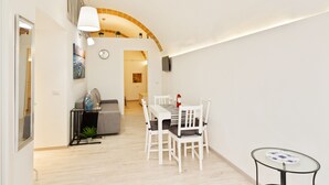 A dining area with a white table and chairs, a small round table with a glass top, and a wall-mounted TV. - San Nicola Casa Clemente Apartment (Bari)