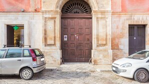 A building with a large, ornate brown door, a small sign with a red circle and a white cross, and a number '18' on the door. - La terrazza sulla Chiesa di San Francesco d'Assisi (Castellana Grotte)
