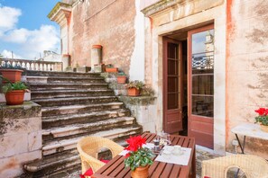 A stone staircase leading to a building entrance, with potted plants and wicker furniture on the landing.