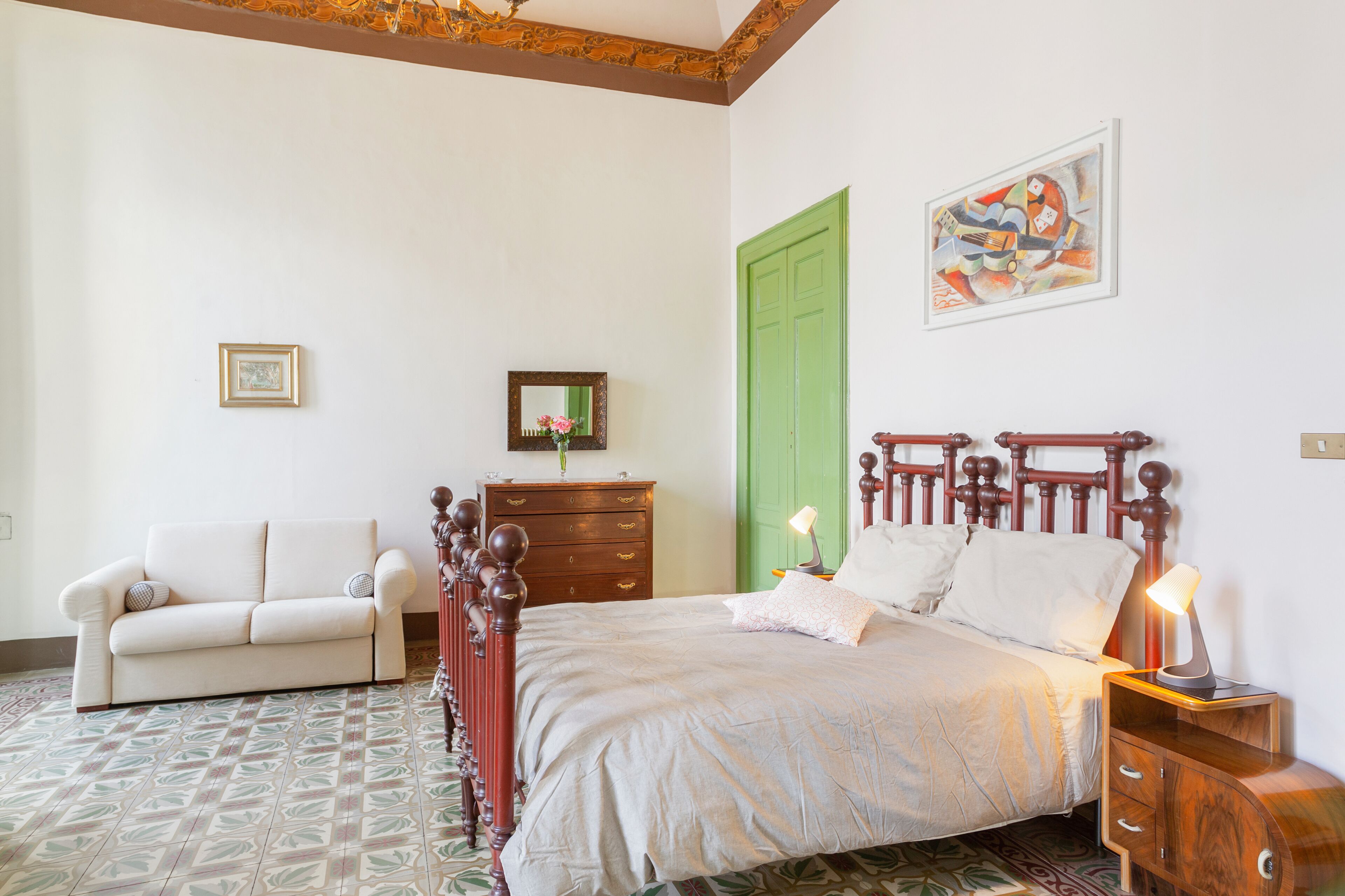 A bedroom with a wooden bed, a green door, a white sofa, and a framed picture on the wall.