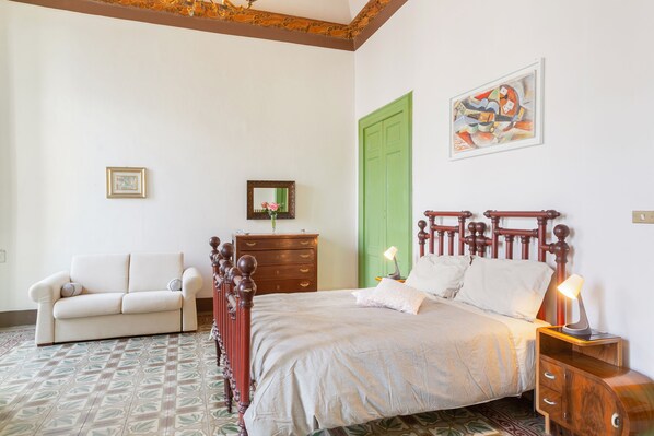 A bedroom with a wooden bed, a green door, a white sofa, and a framed picture on the wall.