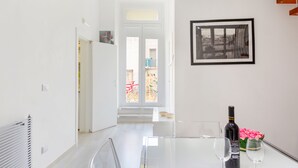 A modern, well-lit room with a glass table, two wine glasses, a bottle of wine, and a framed picture on the wall. - Cute flat in the heart of Monopoli (Monopoli)