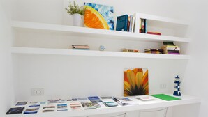 A white shelf with books, a potted plant, and a painting. - Cute flat in the heart of Monopoli (Monopoli)