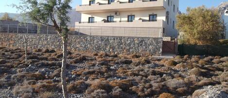 A multi-story building with a flat roof and balconies, surrounded by rocky terrain and sparse vegetation.