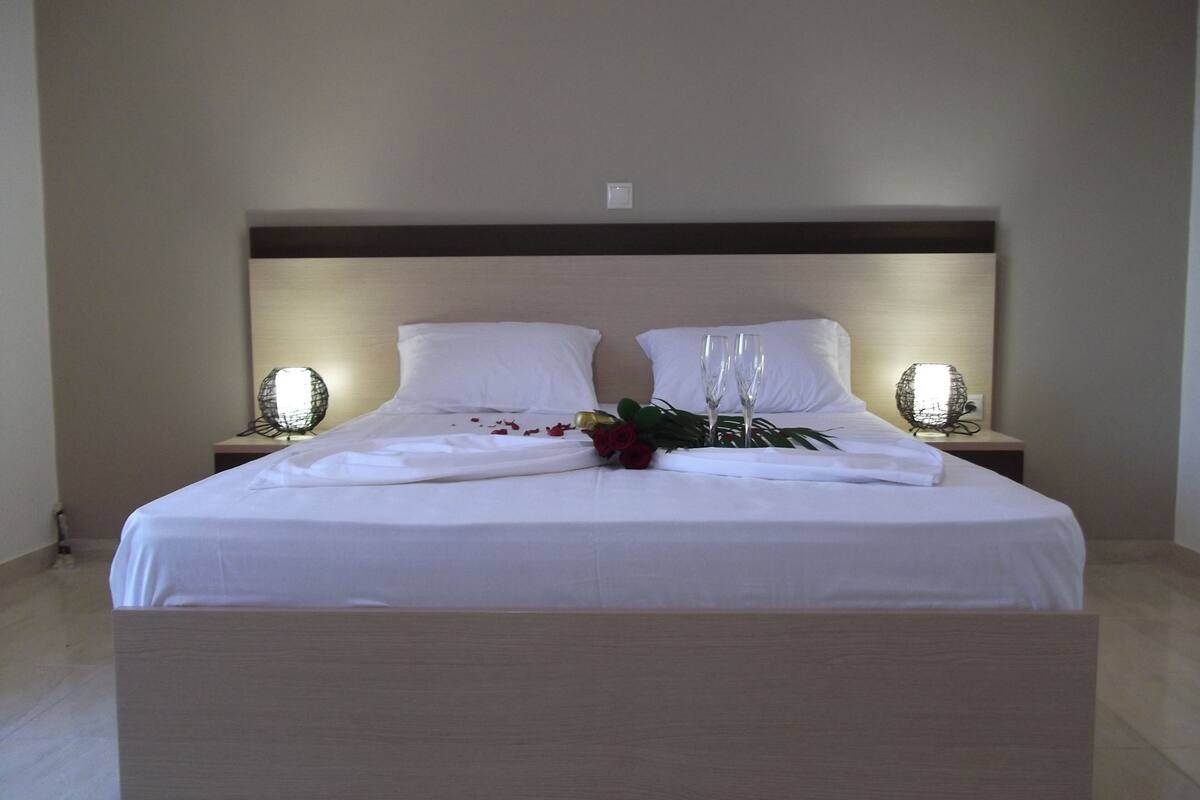 A neatly made bed with white linens, two bedside lamps, and a bouquet of flowers on the bed.