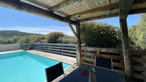 Una terraza de madera con piscina, una silla y un florero con flores.