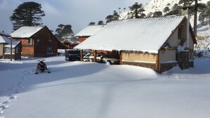 Een besneeuwd dorpje met houten huizen, een geparkeerde auto en een sneeuwscooter.