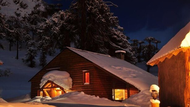 Een houten hut met een sneeuwbedekte dak, omringd door sneeuw en bomen.