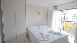 A hotel room with a bed, a wardrobe, a balcony with yellow chairs, and a city view. - PB02 Ap. a 500m do Fiesta Pituba (Salvador)