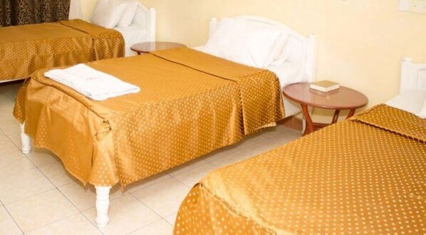 Habitación de hotel con dos camas individuales, cada una con una almohada blanca y una colcha marrón. Hay una pequeña mesa de madera con un libro encima.