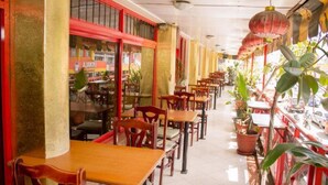 An indoor restaurant with wooden tables and chairs, potted plants, and red-framed windows. - Avenue Suites Hotel (Nakuru)