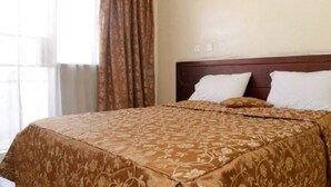 A hotel room with a large bed, a wooden headboard, and a window with curtains. - Avenue Suites Hotel (Nakuru)