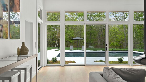 Un interior moderno con un amplio ventanal corredero que da a una zona de piscina, un sofá gris y una barra minimalista.