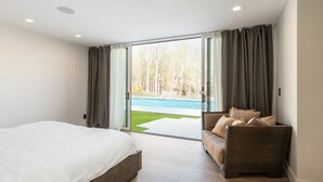 Un dormitorio con una cama grande, un sofá y una puerta corrediza de vidrio que da a una piscina.