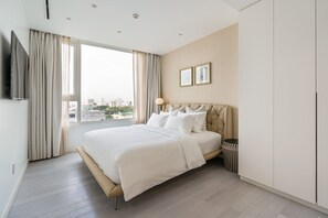 A modern hotel room with a large bed, a TV mounted on the wall, and a view of the city through the window.