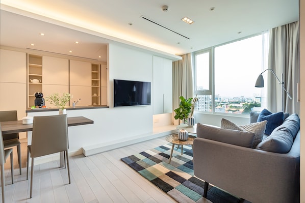 A modern living room with a sofa, a dining area, and a TV mounted on the wall.
