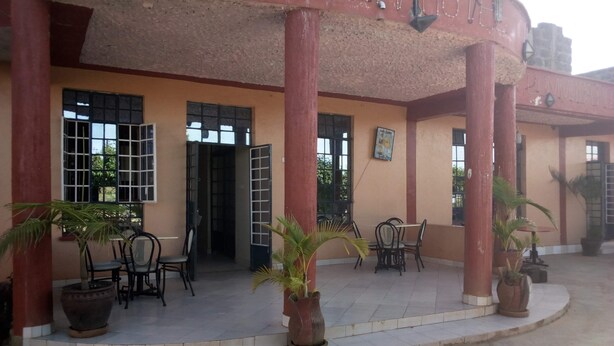A building with a red facade, multiple doors, and outdoor seating with chairs and tables. - Bellview Hotel (Thika)