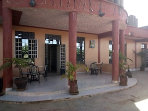 A building with a red facade, multiple doors, and outdoor seating with chairs and tables. - Bellview Hotel (Thika)