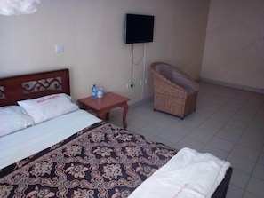A hotel room with a bed, a chair, a television, and a small table with a bottle and a cup. - Bellview Hotel (Thika)