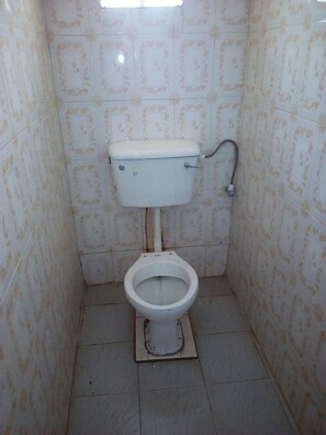 A small, narrow bathroom with a toilet, a wall-mounted flush handle, and tiled walls. - Bellview Hotel (Thika)